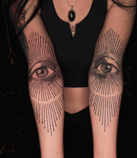 Paired eye tattoos with radiating lines on both forearms
